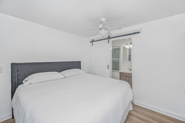 bedroom featuring ceiling fan, ensuite bathroom, light wood-type flooring, and a barn door