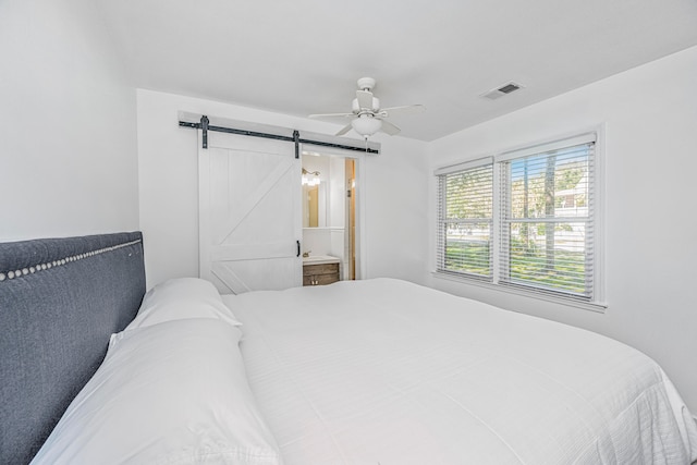 bedroom featuring a barn door, ceiling fan, and ensuite bath