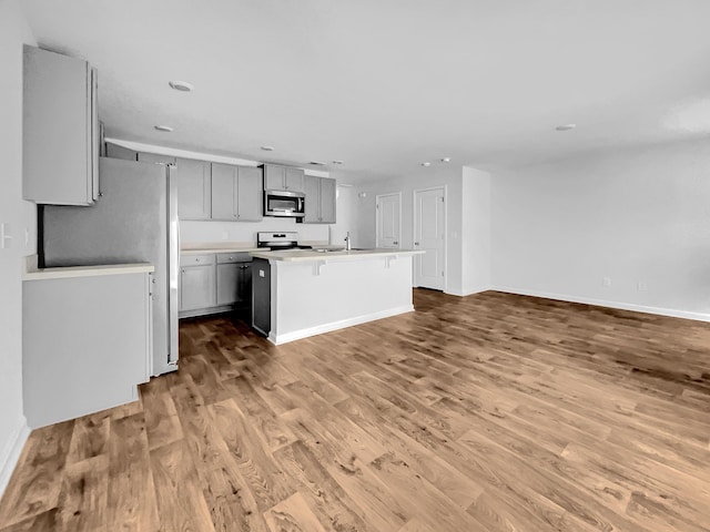 kitchen with appliances with stainless steel finishes, a center island with sink, gray cabinetry, light hardwood / wood-style floors, and sink