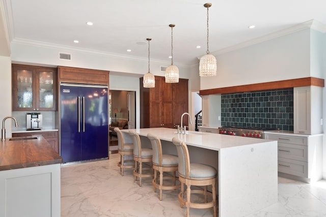 kitchen with built in refrigerator, a center island with sink, light tile floors, backsplash, and sink