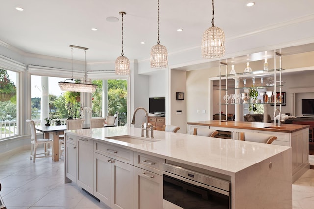 kitchen with hanging light fixtures, sink, a healthy amount of sunlight, a center island with sink, and oven