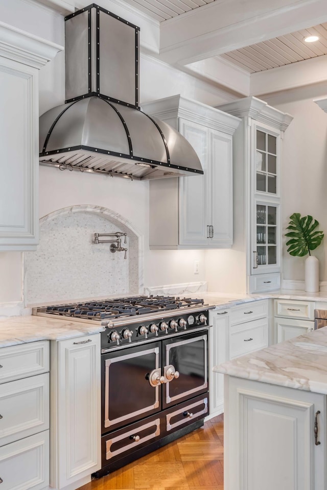 kitchen with glass insert cabinets, white cabinets, ventilation hood, light stone countertops, and double oven range