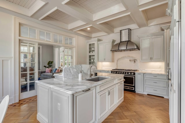 kitchen featuring coffered ceiling, a kitchen island with sink, custom exhaust hood, high end stove, and a sink