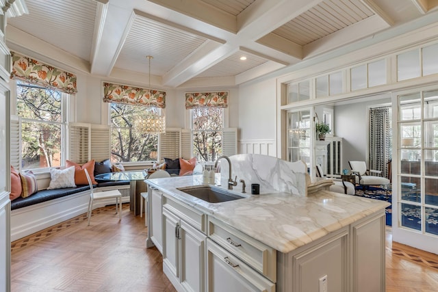 kitchen with coffered ceiling, open floor plan, beamed ceiling, light stone countertops, and a sink