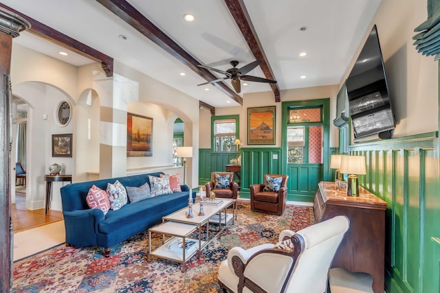 living area featuring arched walkways, wainscoting, beamed ceiling, and recessed lighting