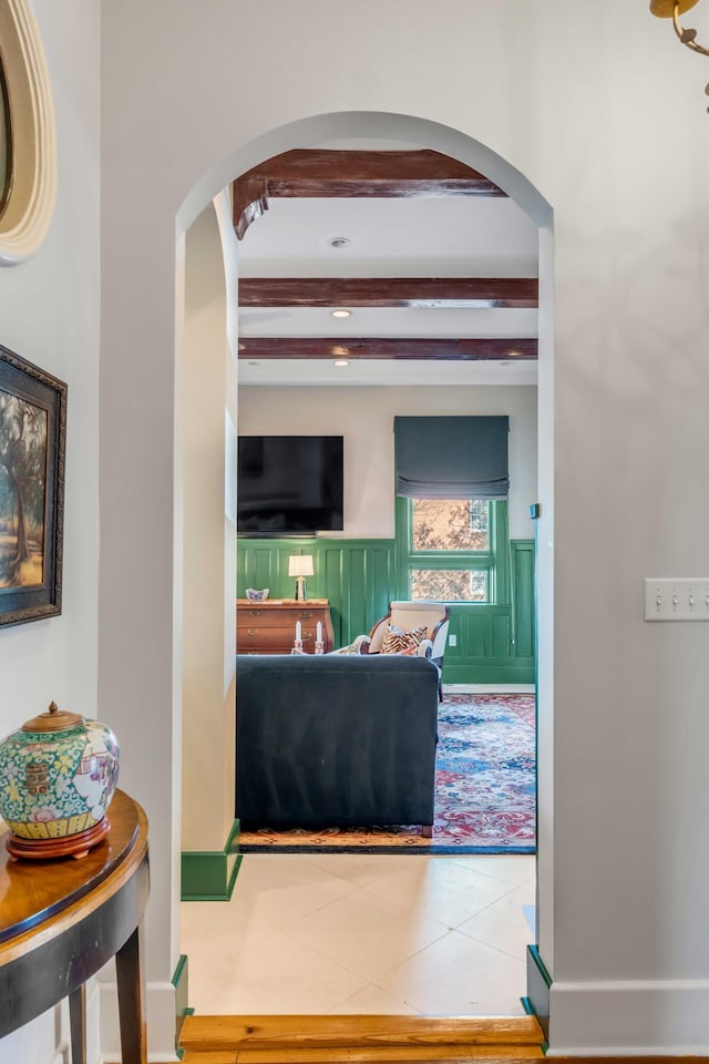 hallway featuring beamed ceiling, wainscoting, and tile patterned floors