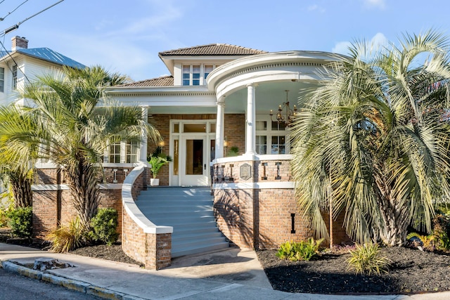 view of front of home with covered porch, a tile roof, and brick siding