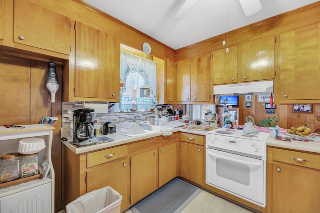 kitchen featuring brown cabinetry, white range with electric cooktop, a sink, light countertops, and under cabinet range hood