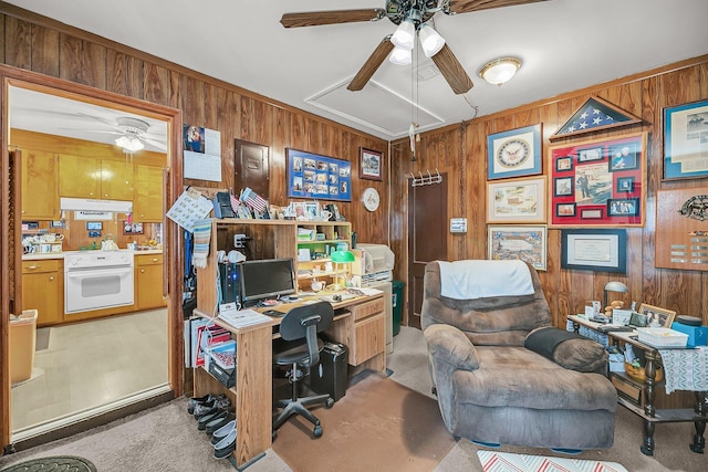 carpeted home office with wooden walls, attic access, and ceiling fan