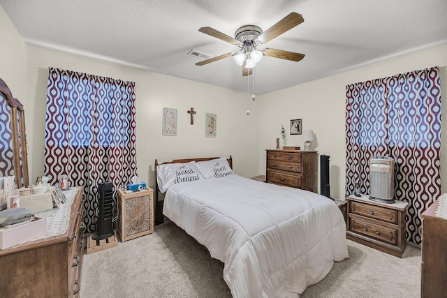 bedroom with a textured ceiling, ceiling fan, visible vents, and light carpet