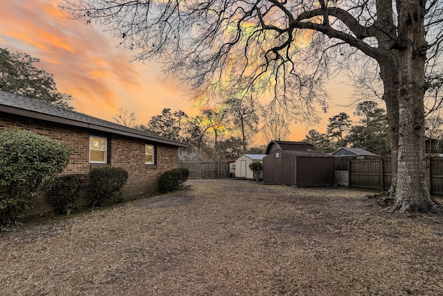 yard at dusk with a storage unit, an outdoor structure, driveway, and fence