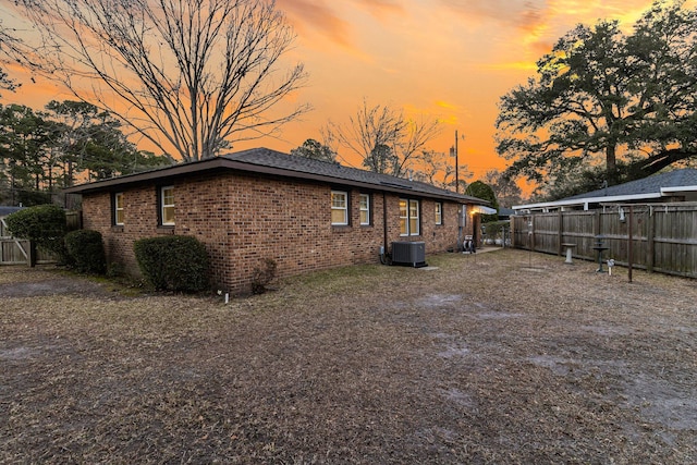 back of property at dusk with central air condition unit, brick siding, and fence