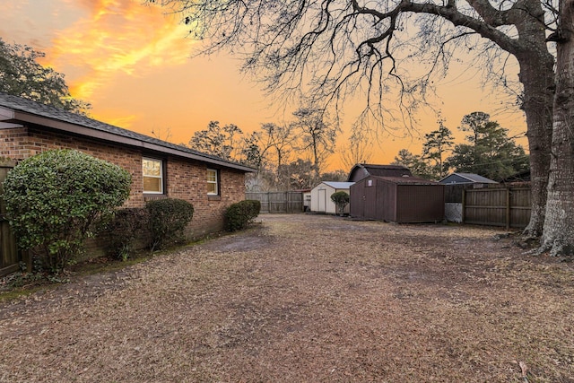 yard at dusk with an outbuilding, a storage shed, and fence