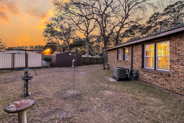 yard at dusk featuring an outbuilding, cooling unit, fence, and a storage unit