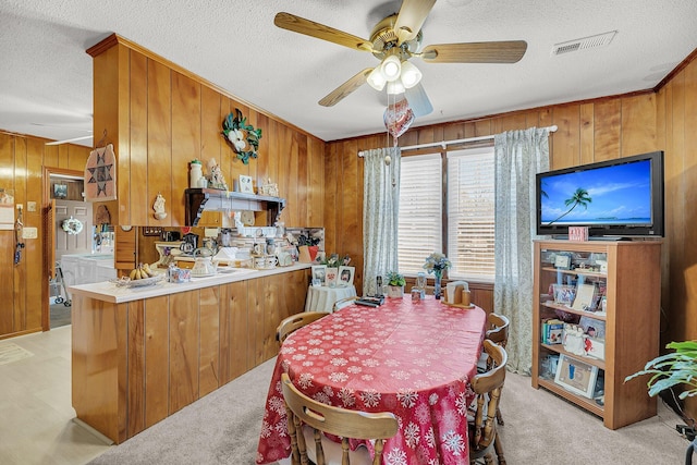 dining area featuring visible vents, ceiling fan, wood walls, light colored carpet, and a textured ceiling