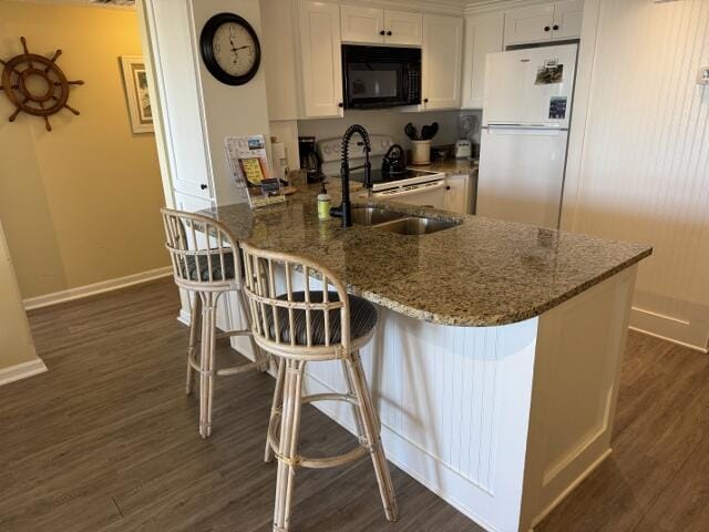 kitchen featuring kitchen peninsula, dark stone counters, a breakfast bar, white appliances, and white cabinets