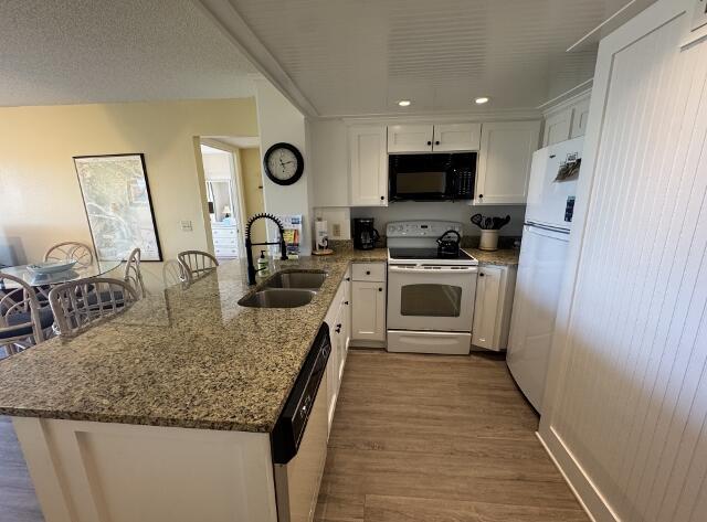 kitchen featuring white cabinetry, sink, light stone countertops, kitchen peninsula, and white appliances