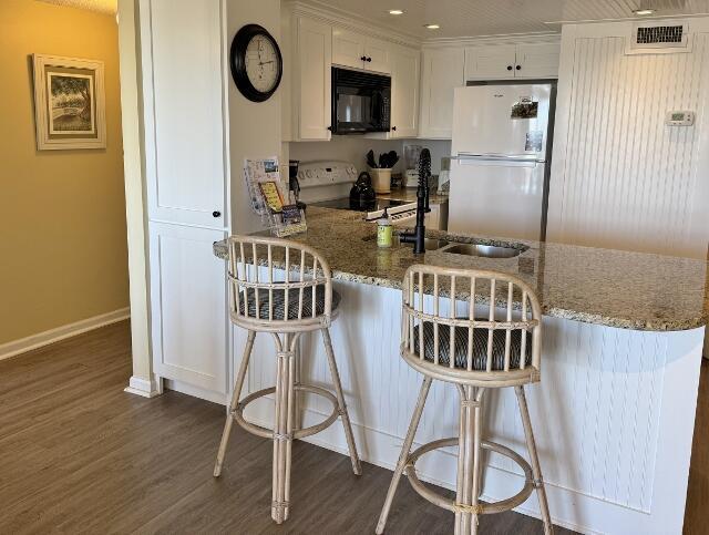 kitchen featuring a breakfast bar, white refrigerator, stone counters, range, and white cabinetry