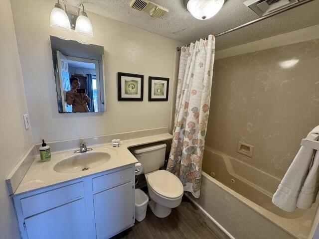 full bathroom with vanity, a textured ceiling, shower / bath combo with shower curtain, hardwood / wood-style flooring, and toilet