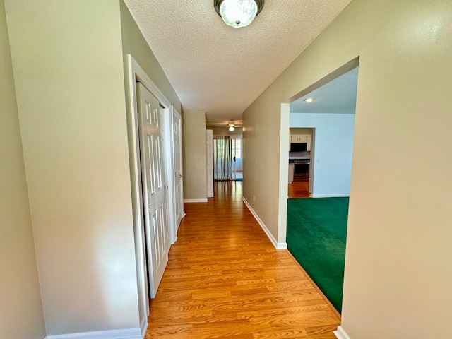 hallway with light hardwood / wood-style flooring and a textured ceiling