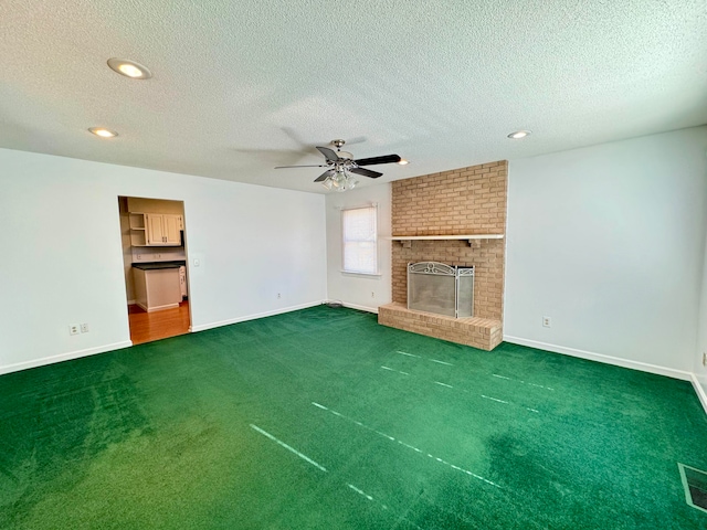 unfurnished living room featuring a textured ceiling, ceiling fan, dark carpet, and a brick fireplace