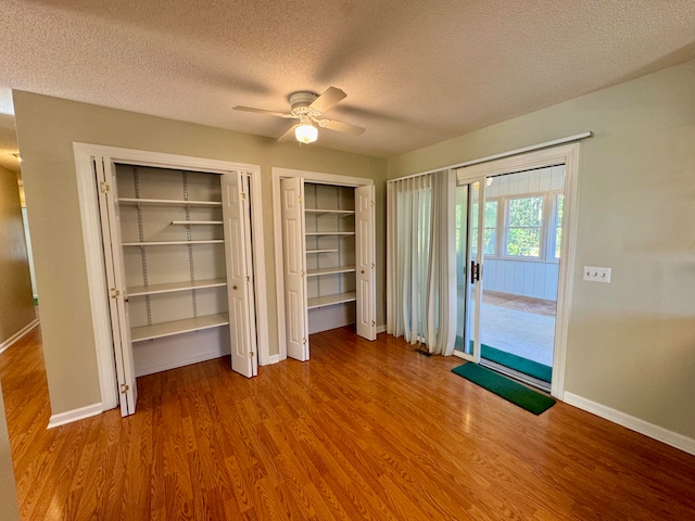 unfurnished bedroom featuring multiple closets, hardwood / wood-style floors, a textured ceiling, and ceiling fan