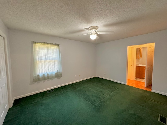 unfurnished bedroom with a textured ceiling, ensuite bath, carpet flooring, and ceiling fan