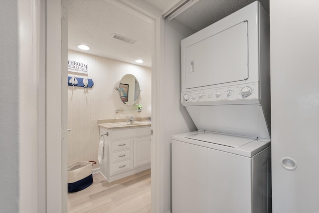 laundry room with stacked washer / dryer, sink, light hardwood / wood-style floors, and a textured ceiling