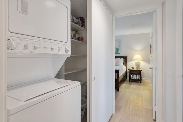 washroom with a textured ceiling, light hardwood / wood-style floors, and stacked washing maching and dryer