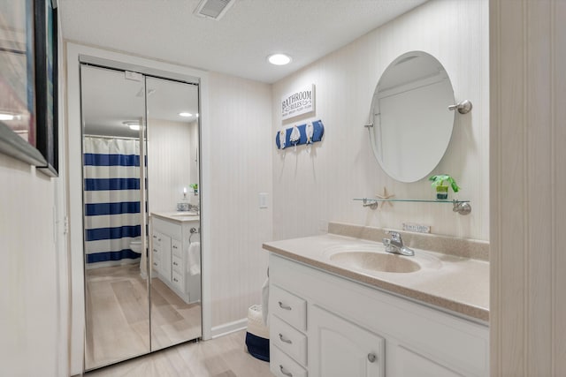 bathroom featuring vanity, wood-type flooring, a textured ceiling, walk in shower, and toilet