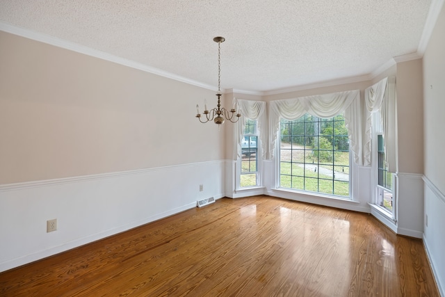 unfurnished room with an inviting chandelier, a textured ceiling, ornamental molding, and hardwood / wood-style floors