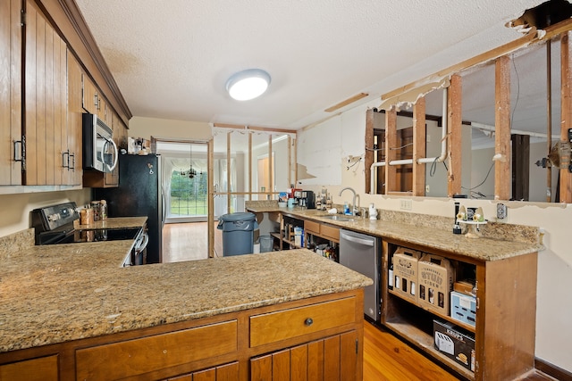 kitchen with appliances with stainless steel finishes, light wood-type flooring, kitchen peninsula, and sink