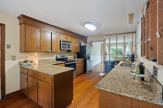 kitchen featuring wood-type flooring, stainless steel appliances, a textured ceiling, sink, and light stone countertops