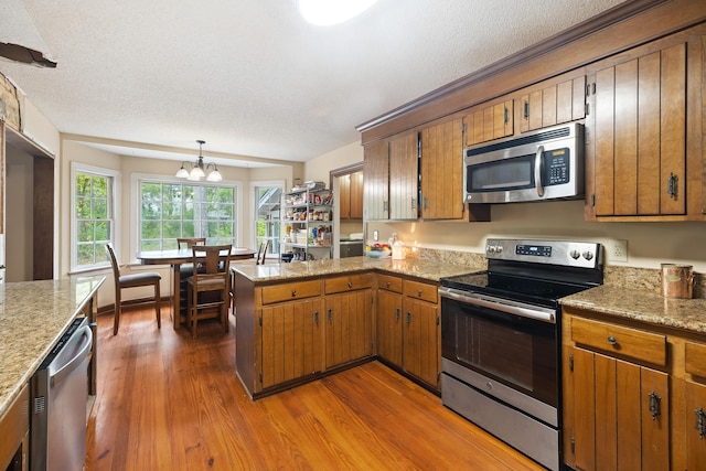 kitchen featuring kitchen peninsula, pendant lighting, dark hardwood / wood-style flooring, stainless steel appliances, and a notable chandelier