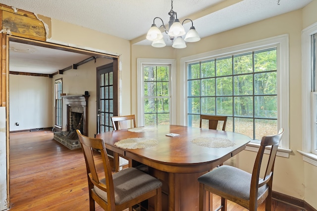 dining room with an inviting chandelier, a stone fireplace, hardwood / wood-style flooring, and a textured ceiling