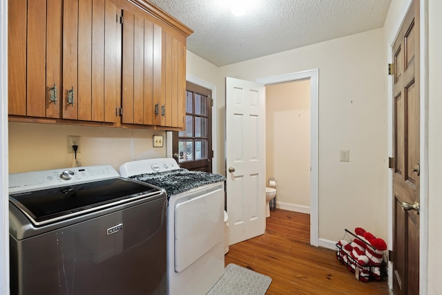 laundry room with a textured ceiling, cabinets, light wood-type flooring, and washing machine and dryer