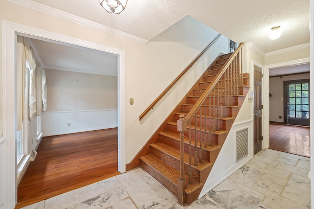 stairway with crown molding, light wood-type flooring, and a textured ceiling