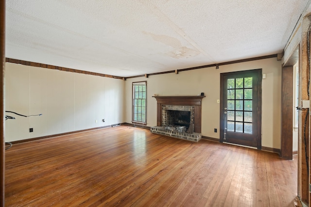 unfurnished living room with a brick fireplace, light hardwood / wood-style flooring, ornamental molding, and a textured ceiling