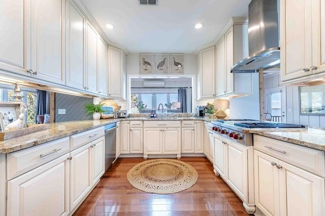 kitchen featuring visible vents, wood finished floors, stainless steel appliances, wall chimney exhaust hood, and a sink