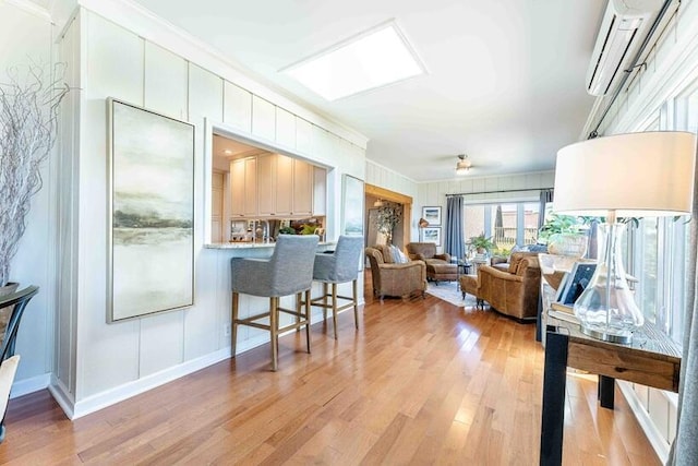 living area featuring crown molding, a ceiling fan, light wood-type flooring, a decorative wall, and an AC wall unit