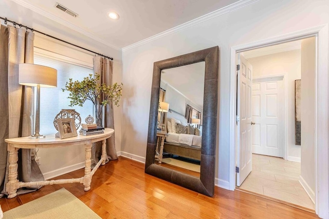 hallway featuring light wood-type flooring, crown molding, baseboards, and visible vents