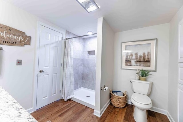bathroom with toilet, baseboards, a tile shower, and wood finished floors