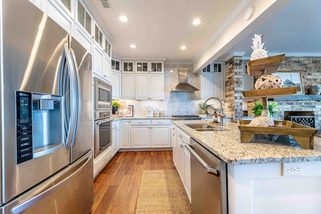 kitchen featuring crown molding, stainless steel appliances, decorative backsplash, a sink, and wall chimney range hood