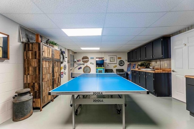 recreation room featuring concrete floors, concrete block wall, and a drop ceiling