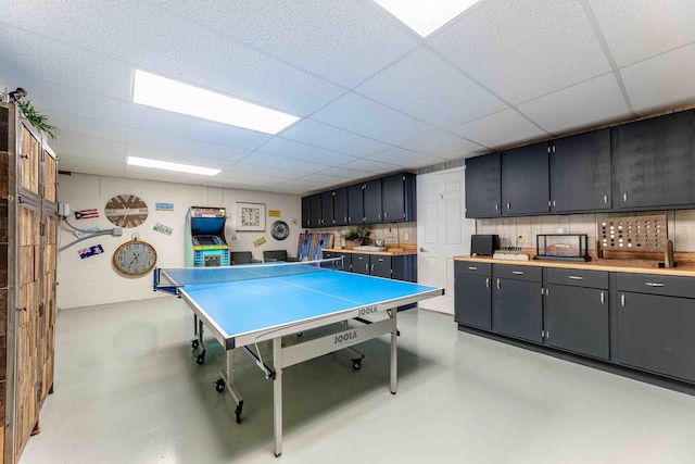 rec room featuring finished concrete flooring, concrete block wall, and a paneled ceiling