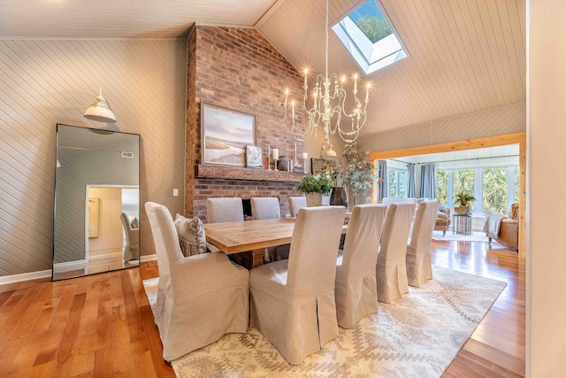 dining area featuring high vaulted ceiling, wood finished floors, a skylight, and a chandelier