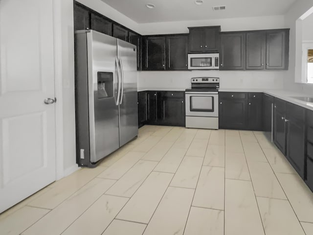 kitchen featuring light countertops, visible vents, appliances with stainless steel finishes, a sink, and dark cabinets