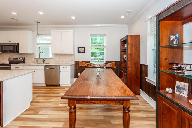 kitchen with light wood-type flooring, crown molding, stainless steel appliances, sink, and hanging light fixtures