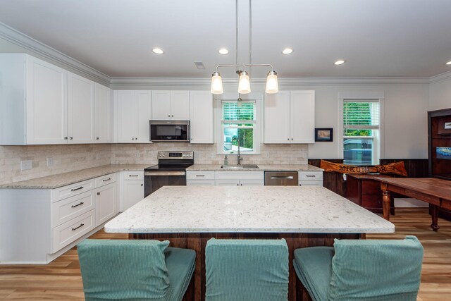 kitchen featuring white cabinetry, decorative light fixtures, a center island, light stone countertops, and appliances with stainless steel finishes