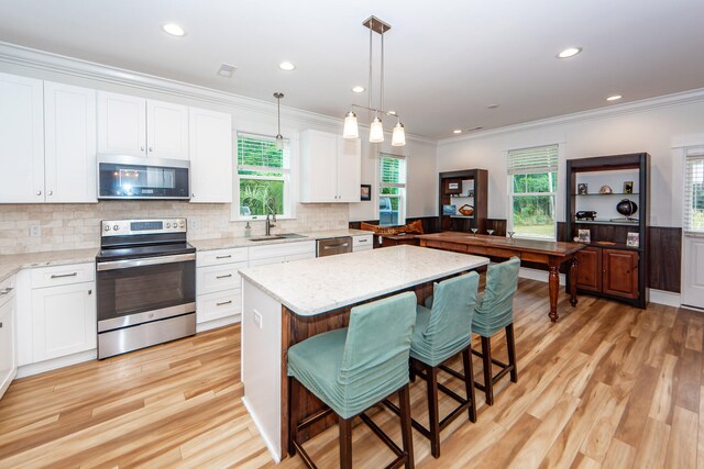 kitchen with light hardwood / wood-style flooring, decorative light fixtures, light stone counters, appliances with stainless steel finishes, and a breakfast bar area